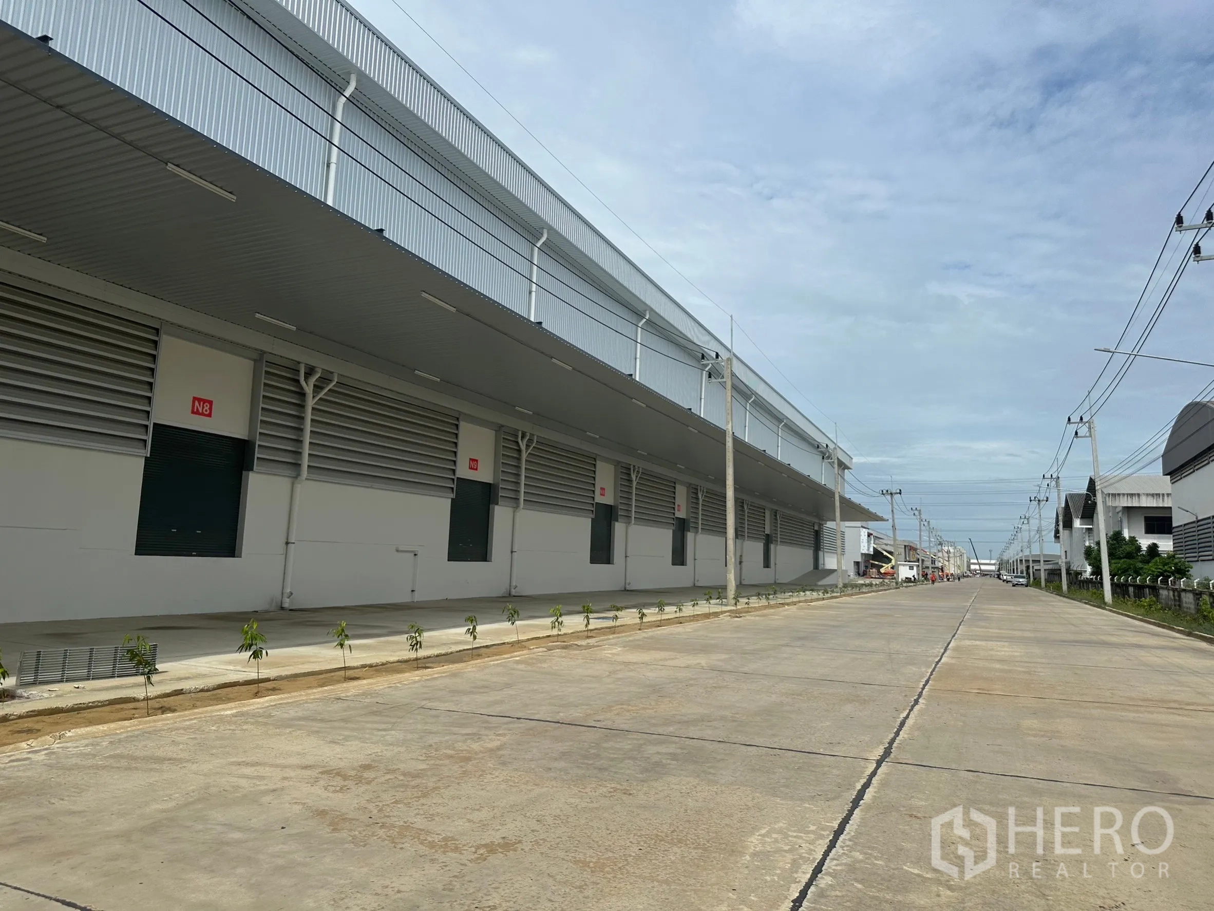 Factory for rent in Khlong Luang, Pathum Thani - Newly built industrial warehouses lining a wide concrete road with overhead power lines in Khlong Luang.