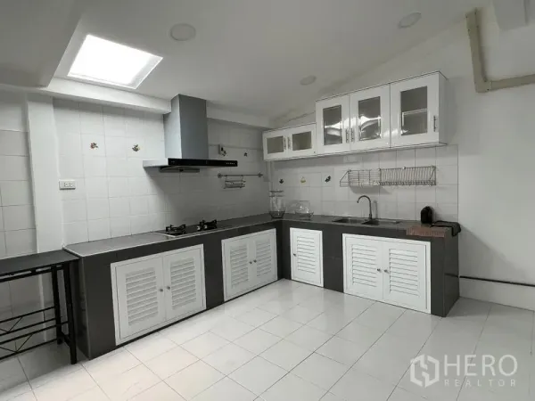 Townhouse for rent in Din Daeng, Bangkok - Bright L-shaped kitchen with gas hob, extractor hood, tiled walls and skylight.