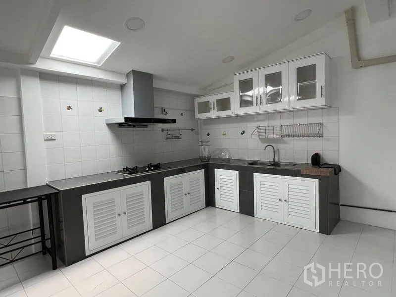 Townhouse for rent in Din Daeng, Bangkok - Bright L-shaped kitchen with gas hob, extractor hood, tiled walls and skylight.