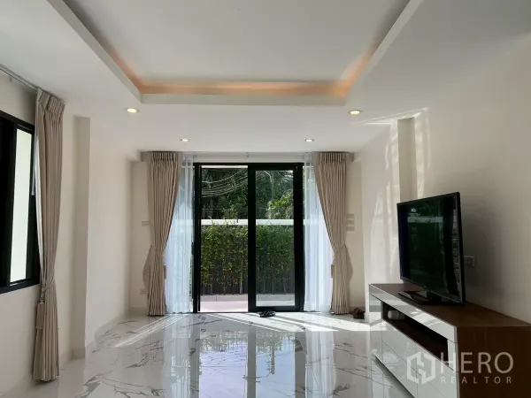 Detached House for rent in Suan Luang, Bangkok - Living room with large sliding doors, TV console, and floor-to-ceiling curtains.