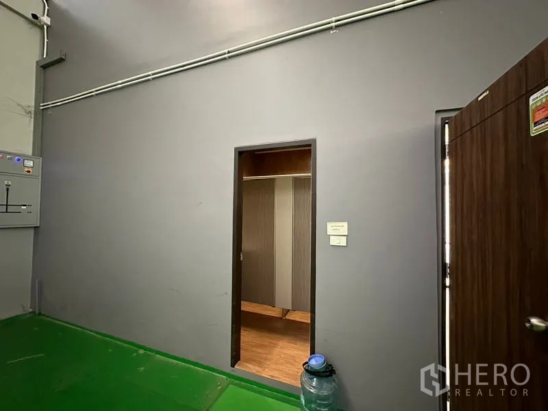 Factory for rent or sale in Lam Luk Ka, Pathum Thani - Warehouse wall with doorway to restroom or locker area next to an electrical control panel.