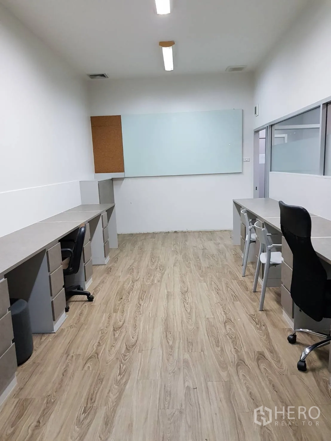 Office Space for rent in Khlong Toei, Bangkok - Private office room with long built-in desks, task chairs, wood-look flooring, and a wall whiteboard.