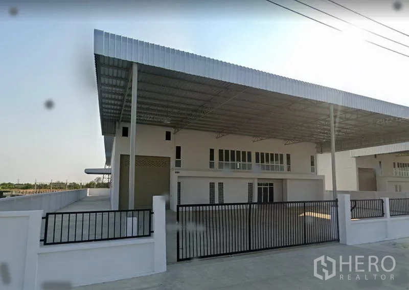 Factory for rent or sale in Bang Bo, Samut Prakan - Angled exterior of the factory showing metal roof cover, deep driveway and black sliding gate.