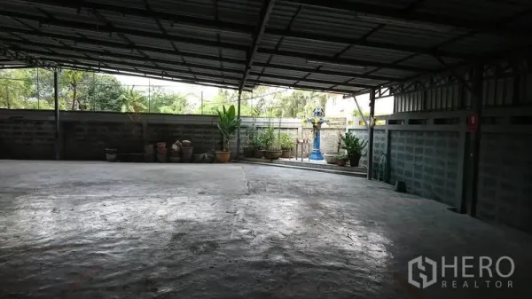 Warehouse for rent in Lak Si, Bangkok - Covered rear yard with concrete floor, low boundary wall, and potted plants.