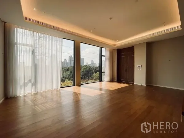 Condominium for sale in Pathum Wan, Bangkok - Spacious living room with floor-to-ceiling windows, cove lighting and park and skyline views.