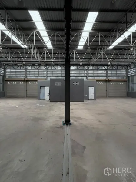 Warehouse for rent in Phra Pradaeng, Samut Prakan - Wide warehouse bay with central support column, skylights, and office blocks facing multiple shutter doors.