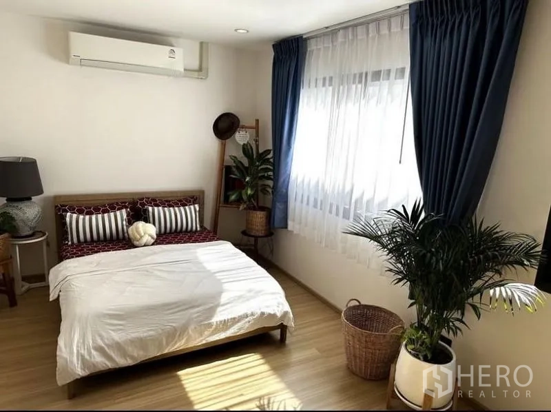 Townhouse for rent in Suan Luang, Bangkok - Guest bedroom with double bed, blue curtains, and potted plants.