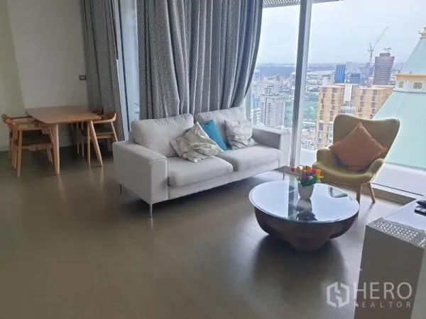Condominium for rent in Pathum Wan, Bangkok - Lounge with sofa, round coffee table, dining set and panoramic city outlook from large windows.