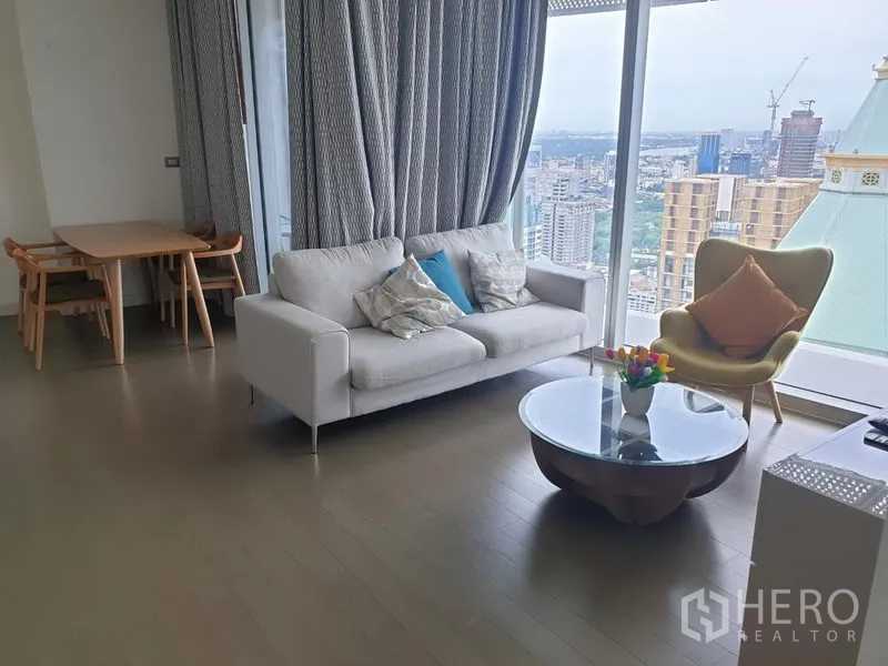 Condominium for rent in Pathum Wan, Bangkok - Lounge with sofa, round coffee table, dining set and panoramic city outlook from large windows.