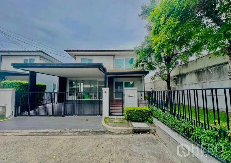 Detached House for sale in Prawet, Bangkok - Front facade of modern two-storey house with metal fence and wide driveway.