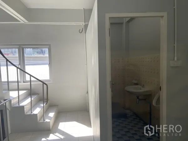 Shophouse for rent in Bang Na, Bangkok - Bright stairwell with windows beside the entrance to a tiled restroom.