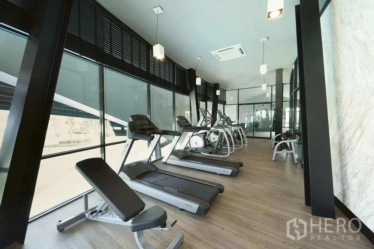 Detached House for rent or sale in Pathum Thani - Gym with treadmills and ellipticals along full-height windows.