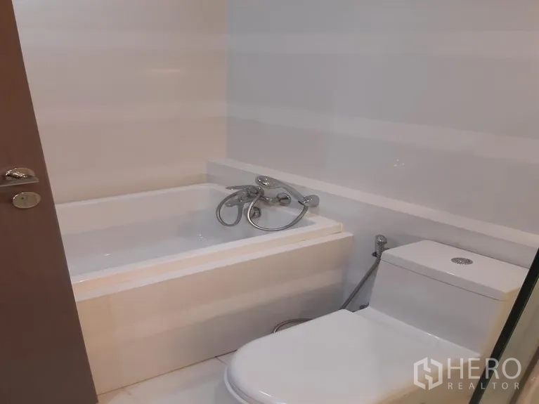 Condominium for rent in Khlong Toei, Bangkok - Bathroom with white bathtub and toilet in a minimalist style.
