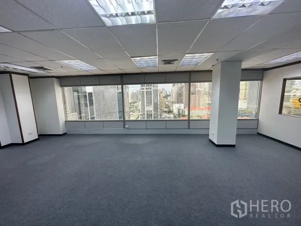 Office Space for rent in Pathum Wan, Bangkok - Open-plan office with carpet flooring, grid ceiling lights, and wide windows overlooking the Bangkok skyline.