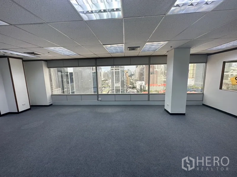 Office Space for rent in Pathum Wan, Bangkok - Open-plan office with carpet flooring, grid ceiling lights, and wide windows overlooking the Bangkok skyline.