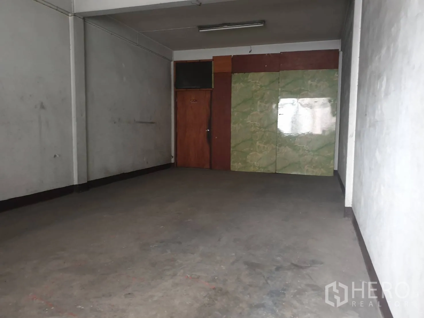 Shophouse for rent in Phra Khanong, Bangkok - Empty concrete room with plain grey walls and a wooden door, suitable for storage or workspace.