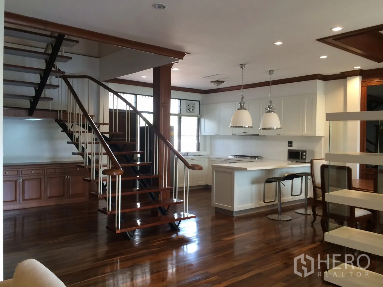 Detached House for rent in Khlong Toei, Bangkok - Bright white kitchen with island, pendant lamps and a floating wooden staircase.