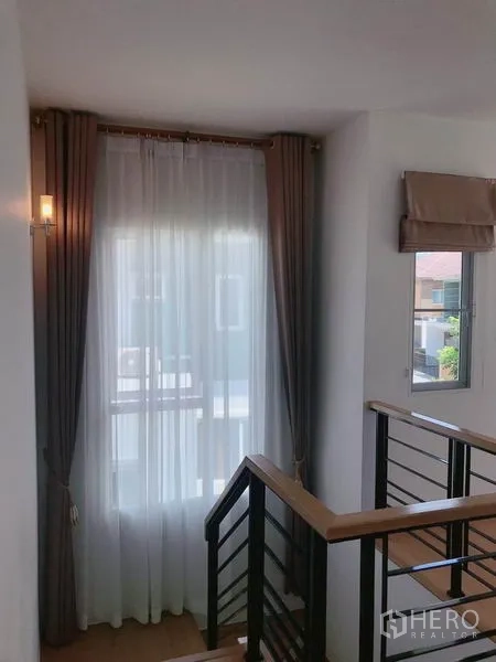 独立式住宅 出售在Suan Luang, Bangkok - 采光良好的楼梯间，窗口与木扶手及薄纱窗帘。