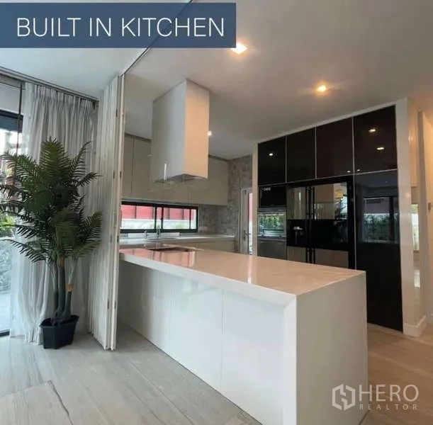 Detached House for sale in Khlong Toei, Bangkok - Modern built-in kitchen with long white island and black cabinetry and fridge.