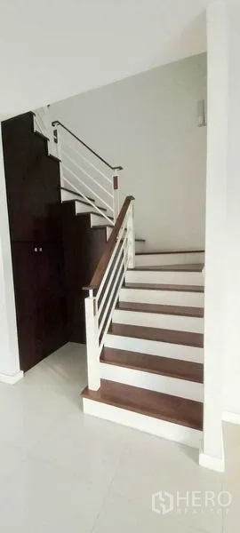Townhouse for sale in Mueang Pathum Thani, Pathum Thani - Staircase with wooden treads, white railings, and storage cabinet beneath.