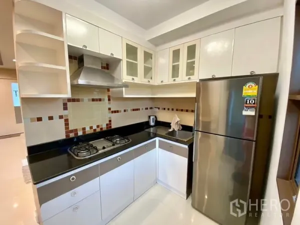Townhouse for rent in Phra Khanong, Bangkok - Modern L-shaped kitchen with gas hob, range hood, glass cabinets and stainless refrigerator.