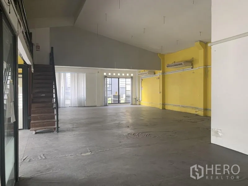 Retail Space for rent in Khlong Toei, Bangkok - Wide retail floor with yellow accent wall, high ceiling, concrete flooring and rear glass doors.