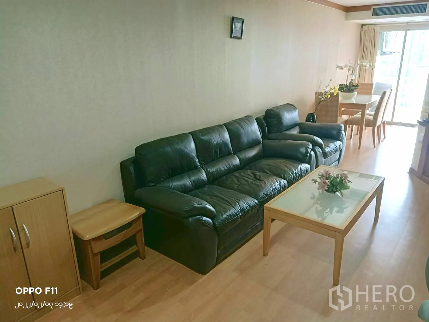 Condominium for rent in Khlong Toei, Bangkok - Living room leading to a windowed dining corner with black sofa and coffee table.