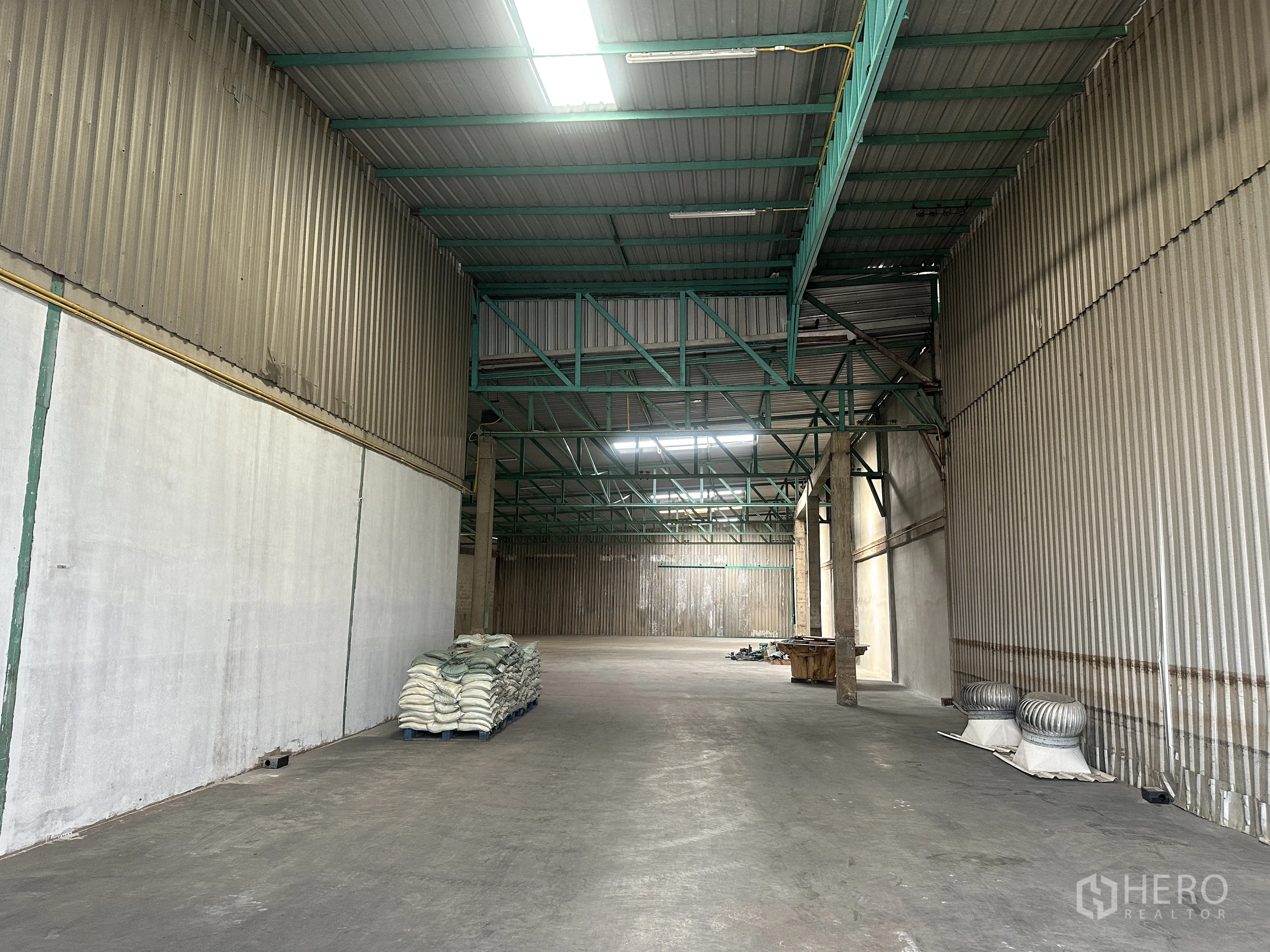 Warehouse for rent in Mueang Pathum Thani, Pathum Thani - Long interior view highlighting clear-span floor area, roof ventilation turbines, and fluorescent lighting.