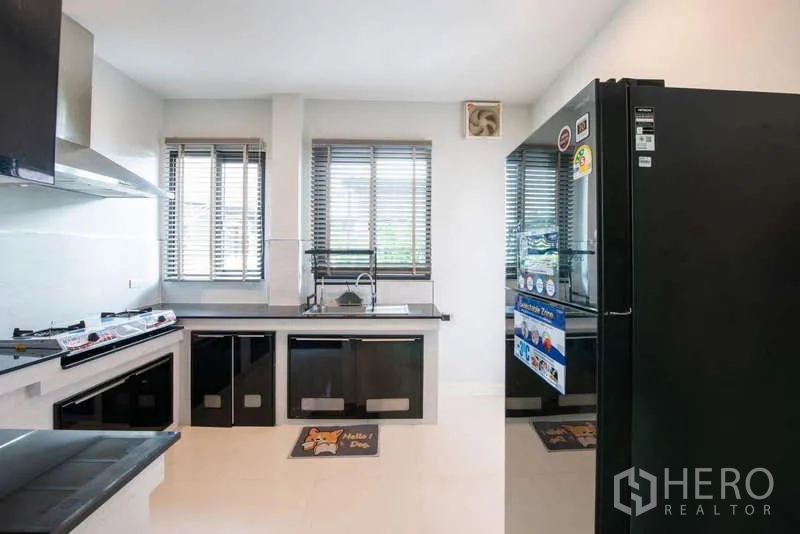 Detached House for rent or sale in Kanchanaburi - Modern kitchen with black cabinetry, gas hob, range hood, and tall refrigerator.