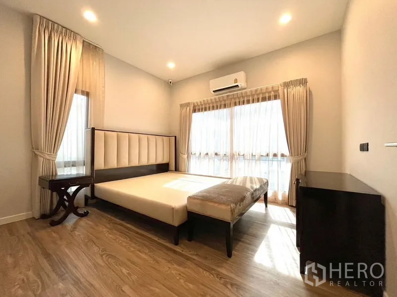 Detached House for rent in Bang Kapi, Bangkok - Sunlit bedroom with padded headboard, bench and air conditioner.