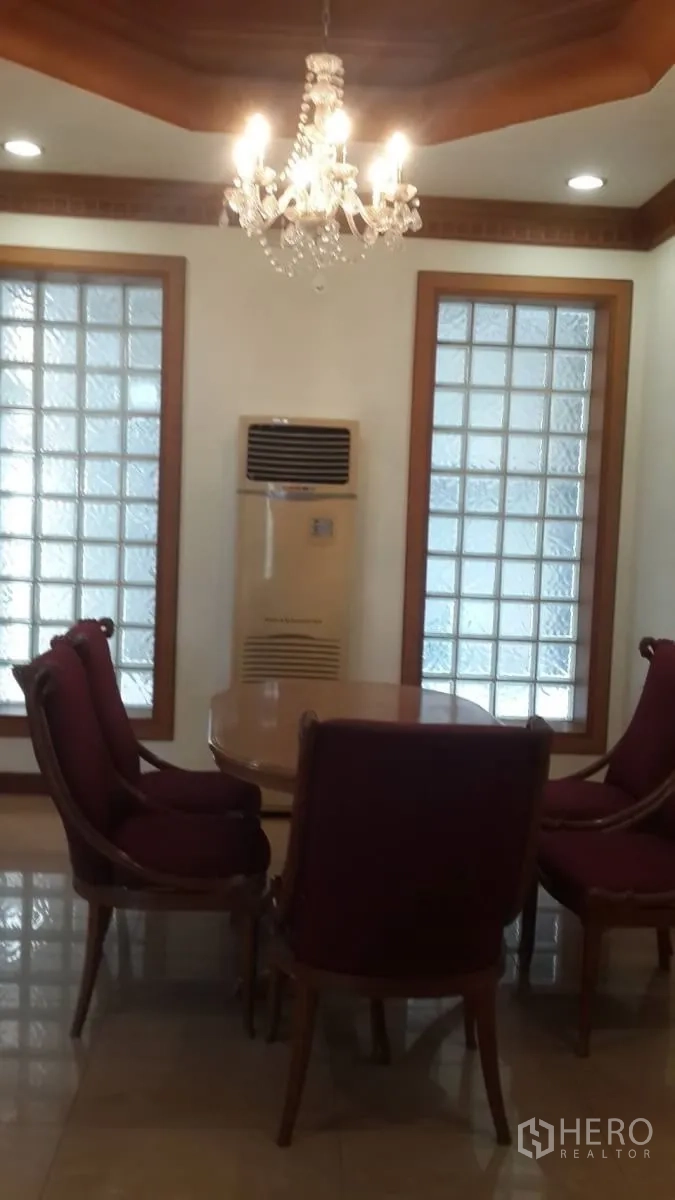 独立式住宅 出租或出售在Huai Khwang, Bangkok - 餐厅一隅，水晶吊灯、玻璃砖窗与经典木椅围绕小餐桌。