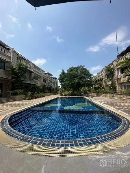 联排别墅 出租在Khlong Toei, Bangkok - 两排联排别墅之间的公共蓝色瓷砖泳池，晴天景色。
