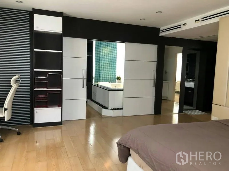 Condominium for rent or sale in Watthana, Bangkok - Spacious master bedroom with wood floors and sliding doors to the ensuite bathroom with storage shelves.