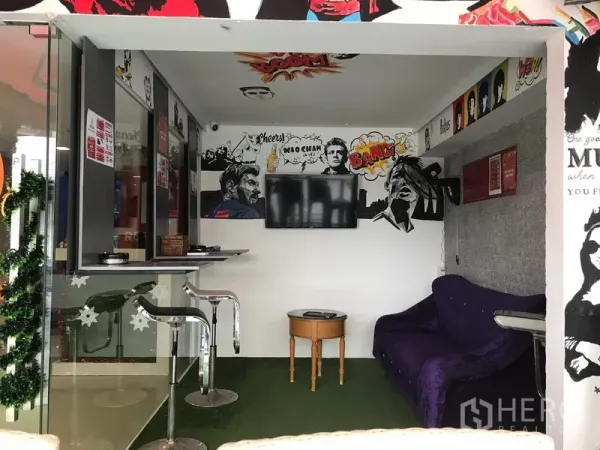 Retail Space for rent in Watthana, Bangkok - Compact interior lounge area with wall‑mounted TV, bar stools, small table and sofa, highlighted by pop‑art wall graphics.