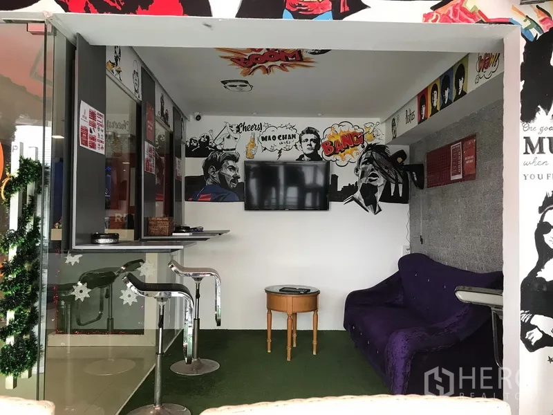 Retail Space for rent in Watthana, Bangkok - Compact interior lounge area with wall‑mounted TV, bar stools, small table and sofa, highlighted by pop‑art wall graphics.