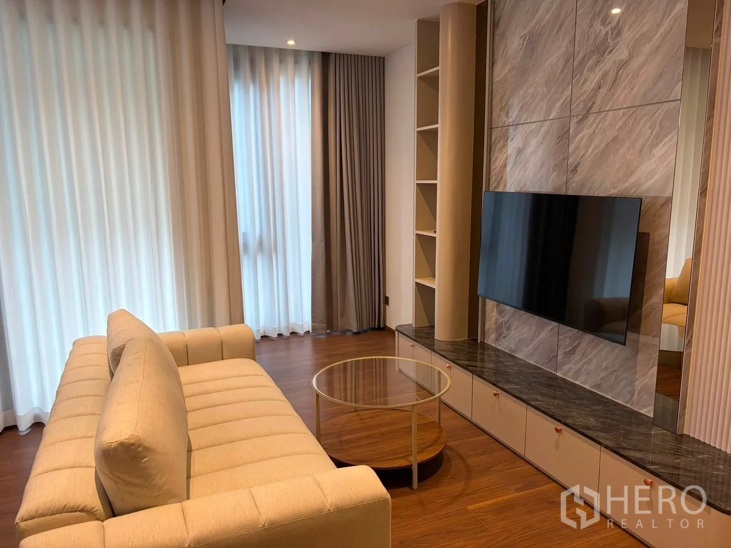 คอนโด for rent in Watthana, Bangkok - ห้องนั่งเล่นมีโซฟาสีเบจ โต๊ะกลางกระจกทรงกลม และหน้าต่างบานใหญ่กับม่านโปร่ง
