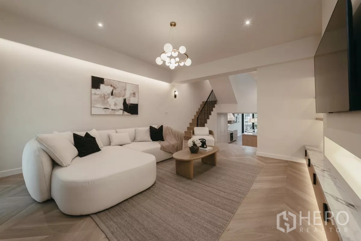 Townhouse for rent in Watthana, Bangkok - Bright living room with large sectional sofa, staircase and recessed lighting.