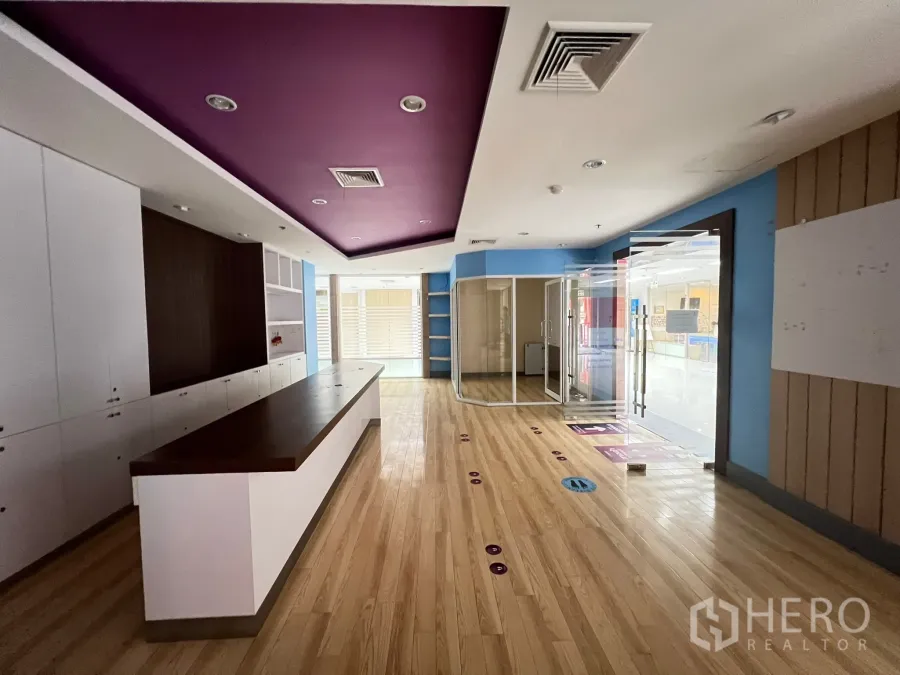 Retail Space for rent - Retail unit interior with long built-in counter, timber flooring, purple recessed ceiling and glass entrance.