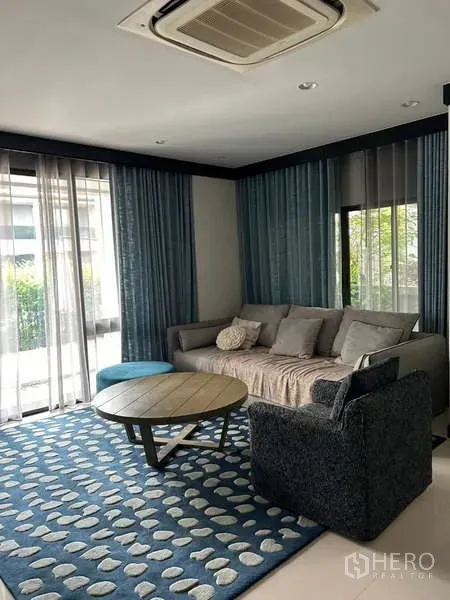 Detached House for rent in Bang Kapi, Bangkok - Cozy living room with sofa, armchair, blue patterned rug and floor‑to‑ceiling windows.