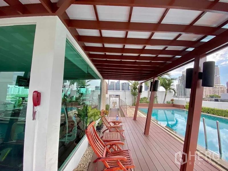 Condominium for rent in Watthana, Bangkok - Rooftop deck beside the pool with wooden pergola, lounge chairs, and city skyline views next to the gym.
