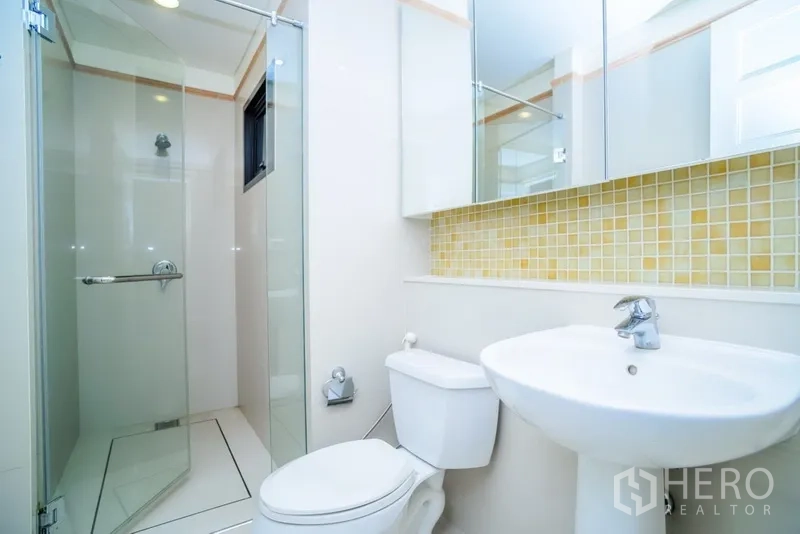Condominium for rent in Khlong Toei, Bangkok - Bright bathroom with glass shower enclosure, pedestal sink, toilet and a mosaic backsplash.