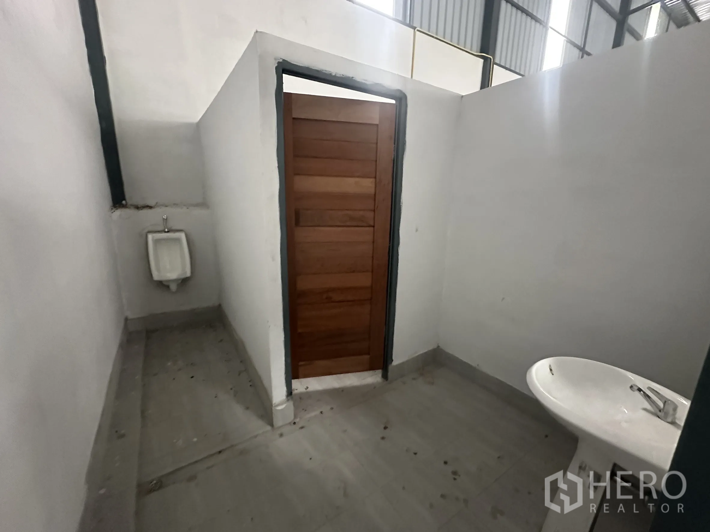 Warehouse for rent in Lam Luk Ka, Pathum Thani - Simple warehouse restroom with sink, urinal and wooden door.