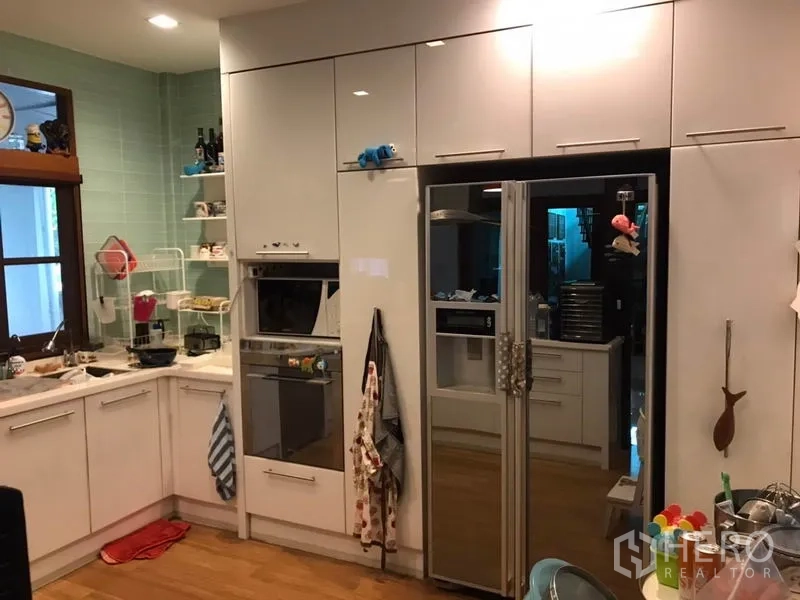 Detached House for sale in Lat Phrao, Bangkok - Built-in oven and double-door refrigerator integrated into sleek white kitchen cabinets.