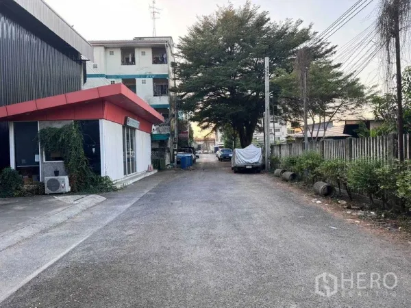 Warehouse for rent in Lat Phrao, Bangkok - Quiet lane outside the warehouse showing a red-roof office, trees and street parking.