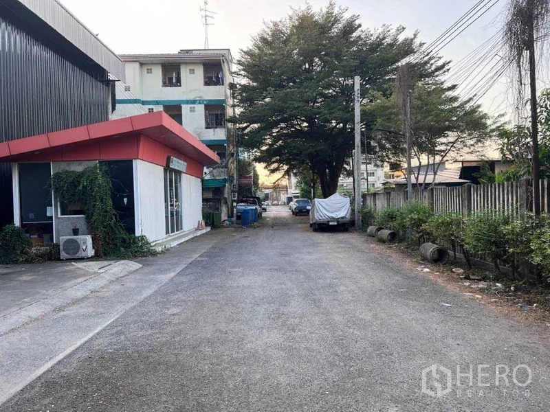Warehouse for rent in Lat Phrao, Bangkok - Quiet lane outside the warehouse showing a red-roof office, trees and street parking.