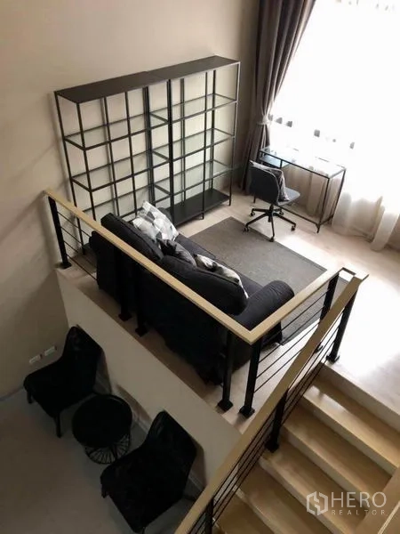 Townhouse for rent in Suan Luang, Bangkok - Aerial view of the mezzanine living nook with sofa, desk and shelving by a tall window.