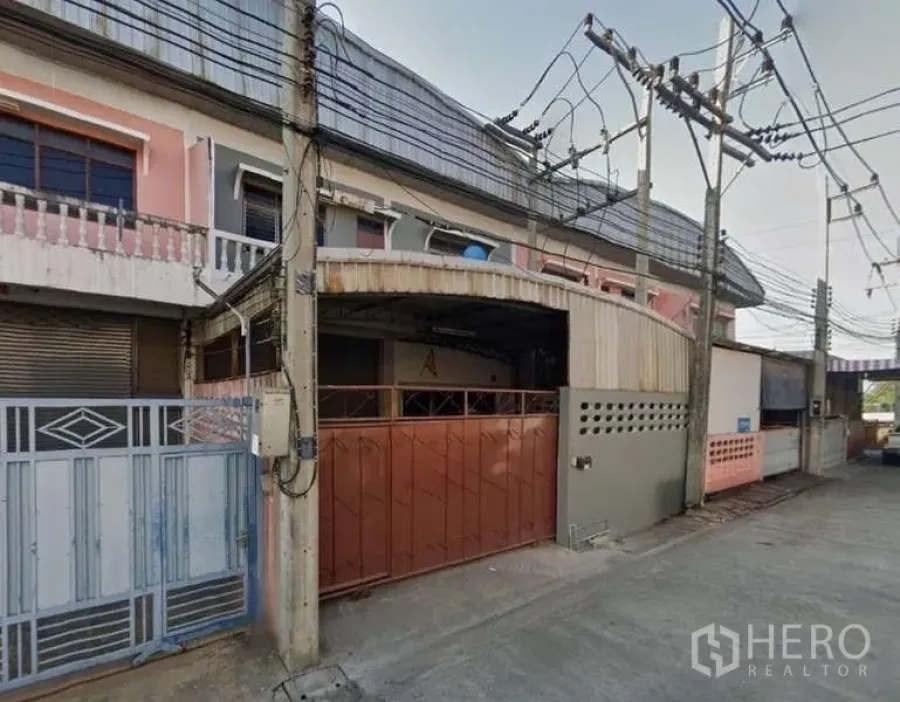 Warehouse for rent in Mueang Samut Sakhon, Samut Sakhon - Covered loading bay with brown metal gate along a quiet concrete lane and overhead power lines.