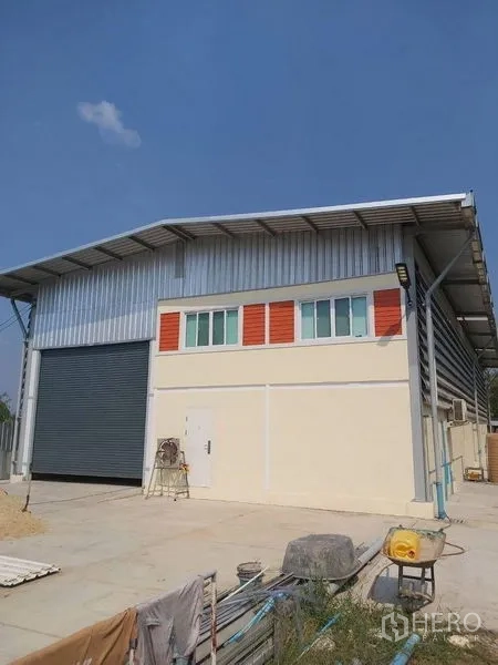 Warehouse for rent in Lam Luk Ka, Pathum Thani - Angle view of warehouse exterior with metal roof and ample yard space.