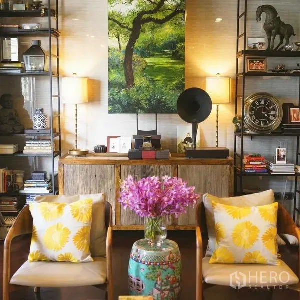 Condominium for sale in Pathum Wan, Bangkok - Warm living area with built-in shelves, twin lamps, framed artwork and fresh flowers on a table.