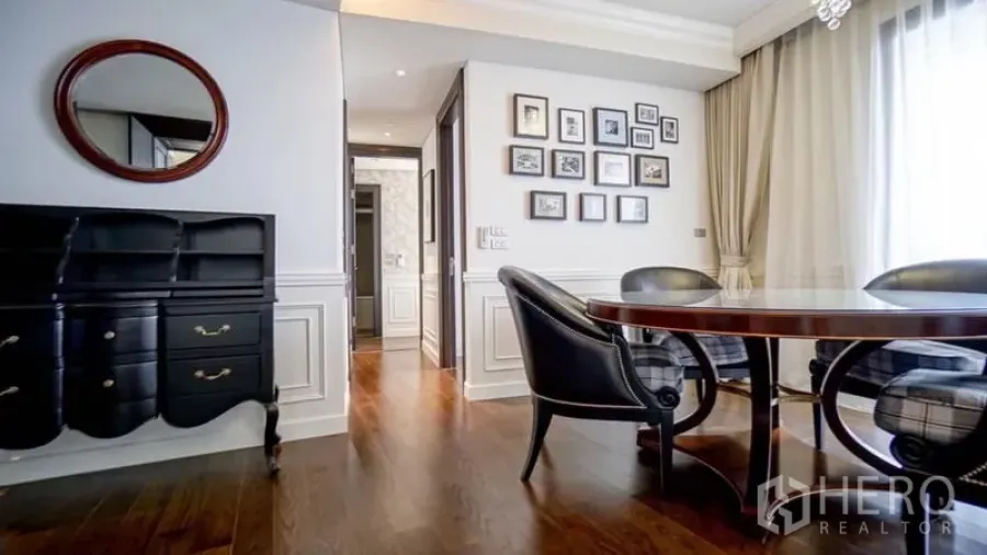 Condominium for rent or sale in Khlong Toei, Bangkok - Elegant dining nook with round wood table, black chairs, gallery wall and wainscoting on hardwood floors.